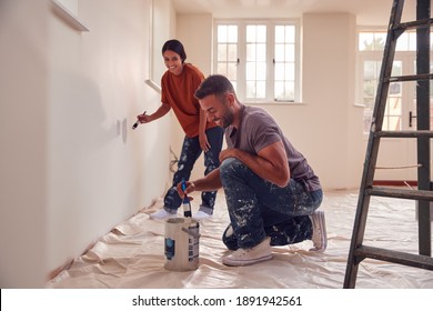 Couple Painting Test Squares On Wall As They Decorate Room In New Home Together