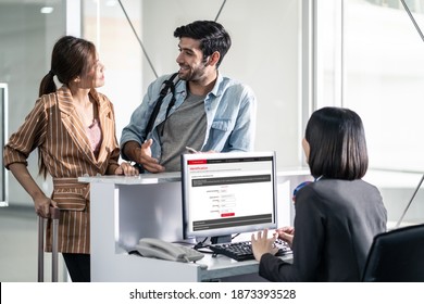 Couple Passengers Talking To Check In Airline Staff In Airport Terminal Building Before Boarding On The Airplane. Asian Woman And Caucasian Man Feeling Happy To Go To Travel By Plane Transportation.