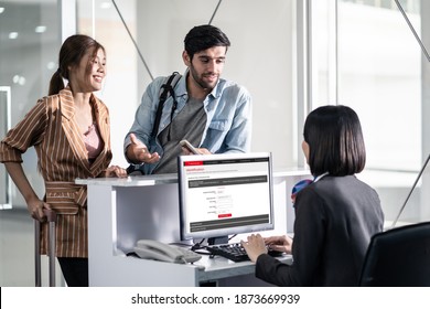 Couple Passengers Talking To Check In Airline Staff In Airport Terminal Building Before Boarding On The Airplane. Asian Woman And Caucasian Man Feeling Happy To Go To Travel By Plane Transportation.