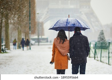 Couple passing by the Eiffel tower in Paris on a day with heavy snow. Unusual weather conditions in Paris, France - Powered by Shutterstock