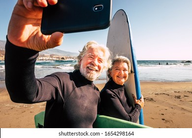 couple of pensioners seniors taking a selfie together at the beach with their wetsuits and surfboards - mature people learning surfing - Powered by Shutterstock