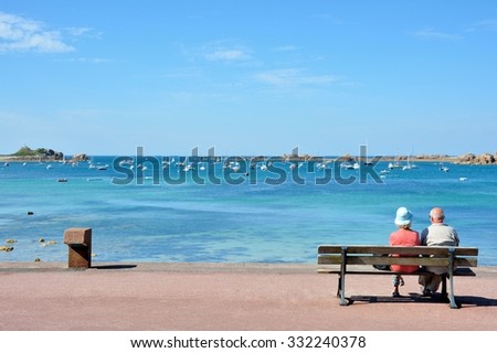A couple of pensioners are waiting on a bench in front of the sea in Brittany