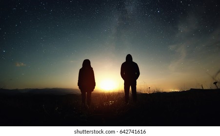 A couple of people man and woman stand at the sunset of the moon under the starry sky with bright stars and a milky way. Silhouetted photo against the starry night sky