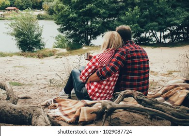 a couple of people in the plaid shirts sitting near the river on picnic and drinking tea - Powered by Shutterstock