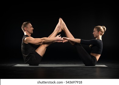 Couple Performing Acroyoga Buddy Boat Pose On Yoga Mat Isolated On Black