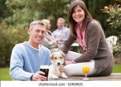 Couple With Pet Dog Outdoors Enjoying Drink In Pub Garden