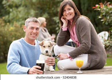 Couple With Pet Dog Outdoors Enjoying Drink In Pub Garden