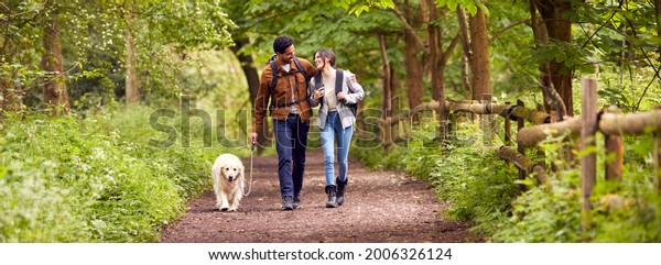 Couple With Pet Golden Retriever Dog Hiking\
Along Path Through Trees In\
Countryside