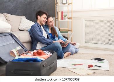 Couple Planning Vacation Trip, Man And Woman Browsing On Laptop,looking For Interesting Travel, Sitting At Home With Packed Suitcase, Copy Space