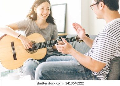 Couple Playing Acoustic Guitar,sing Folk Song Together Sitting On Sofa At Home.concept For Happy Moments Of Young Lovers,family.music And Art Therapy For People With Stress.asian Man,women Relax Time 