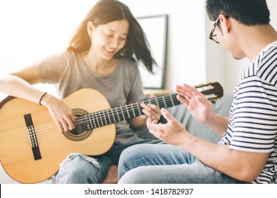 Couple Playing Acoustic Guitar,sing Folk Song Together Sitting On Sofa At Home.concept For Happy Moments Of Young Lovers,family.music And Art Therapy For People With Stress.asian Man,women Relax Time 