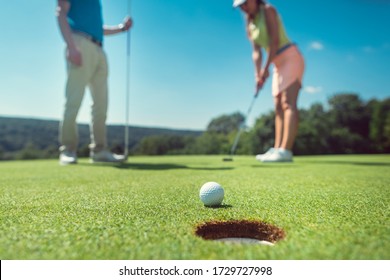 Couple Playing Golf With The Woman On Green To Hole In While Her Partner Is Watching