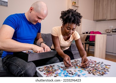 A couple playing with a jigsaw puzzle at home, on a white wooden table. Putting things together and solving problems. Fun and diversity in friendship. - Shutterstock ID 2233296423