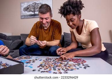 A couple playing with a jigsaw puzzle at home, on a white wooden table. Putting things together and solving problems. Fun and diversity in friendship. - Shutterstock ID 2233296429