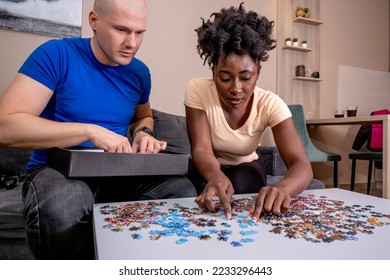 A couple playing with a jigsaw puzzle at home, on a white wooden table. Putting things together and solving problems. Fun and diversity in friendship. - Shutterstock ID 2233296443