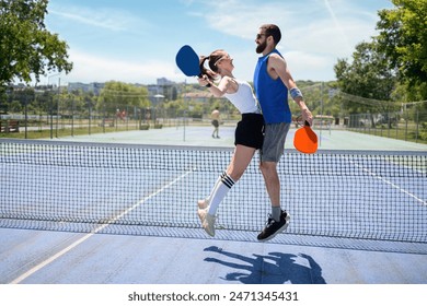 Couple playing pickleball at daylight. Celebrating victory. Outdoor sport leisure activity. Bright blue sky - Powered by Shutterstock