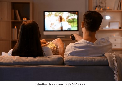 Couple with popcorn watching TV at home in evening - Powered by Shutterstock