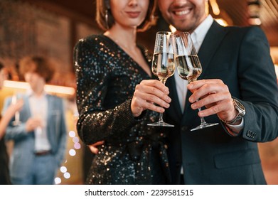 Couple is posing. Group of people in beautiful elegant clothes are celebrating New Year indoors together.