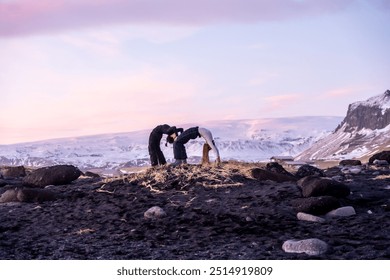 A couple is posing for a picture on a rocky beach. The sky is pink and the sun is setting - Powered by Shutterstock