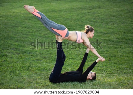 The couple practices acro yoga in the park on the grass