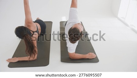 A couple practices a synchronized side plank yoga pose on mats in a bright studio, focusing on core strength and balance to promote a healthy lifestyle.