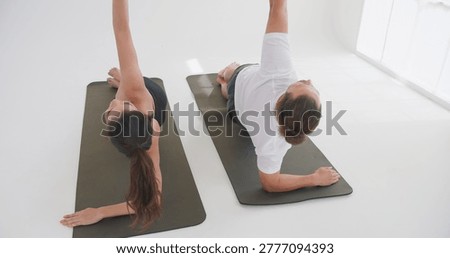 A couple practices a synchronized side plank yoga pose on mats in a bright studio, focusing on core strength and balance to promote a healthy lifestyle.