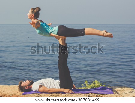Couple practicing acroyoga in the early morning at sea coast, girl lying on the mens feets