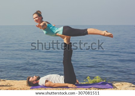 Couple practicing acroyoga in the early morning at sea coast, girl sitting on the mens feets