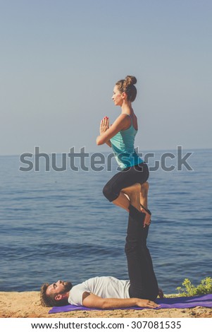 Couple practicing acroyoga in the morning at sea coast, girl sitting on the mens feets