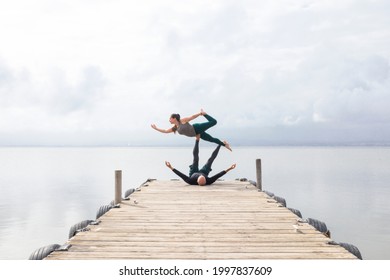 Couple practicing acroyoga on a wooden dock on a lake - Powered by Shutterstock