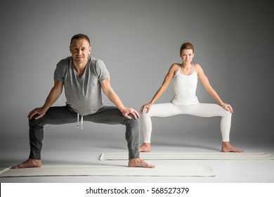 Couple Practicing Yoga Doing Sumo Squat Pose Isolated On Grey