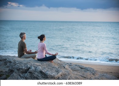 Couple practicing yoga at sunrise on the beach facing the sea - Powered by Shutterstock
