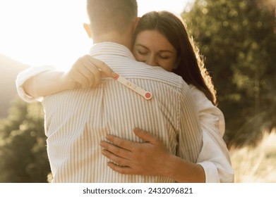 a couple with a pregnancy test hugs while outdoors. happy family concept. husband and wife are expecting a child. pregnancy test - Powered by Shutterstock