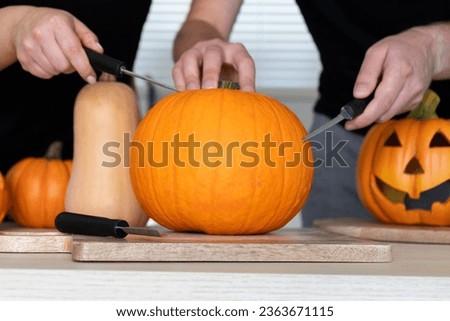 Couple preparing to carve Halloween pumpkins, spooky Jack-o'-lantern cut out. Man and woman standing behind uncarved pumpkin on a table. They holding carving tools, knives, carvers, saw knife blades.