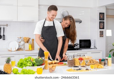 Couple preparing healthy food in kitchen.  Man cutting apple fruit on chopping board, woman hugging and standing behind his couple. Healthy food and home cooking together concept - Powered by Shutterstock