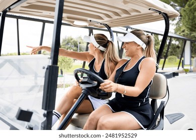 A couple of pretty blonde girls are having fun one day on a golf course.The young women are sitting in a golf cart while they point out where the ball has gone.Blonde women playing golf on a sunny day - Powered by Shutterstock