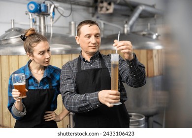 Couple of professional brewmasters standing on background of fermenters at brewery, using test tube and hydrometer to check alcoholic content in craft beer - Powered by Shutterstock