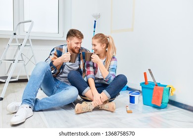 Couple Of Professional Painters Redo A Living Room, Have A Rest With A Cup Of Tea, Sitting Among Paint Tools And Accessories During The Break