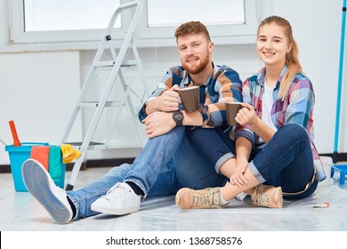 Couple Of Professional Painters Redo A Living Room, Have A Rest With A Cup Of Tea, Sitting Among Paint Tools And Accessories During The Break