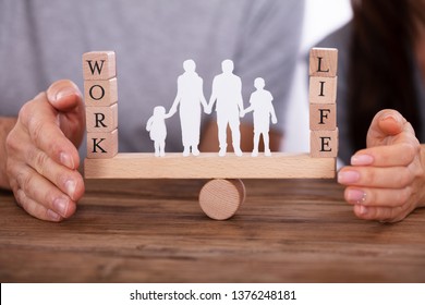 Couple Protecting Work And Life Balance With Family Figures Standing Between Them On Seesaw