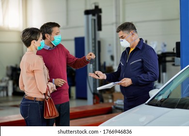 Couple with protective face masks giving car key to their auto repairman in a workshop.  - Powered by Shutterstock