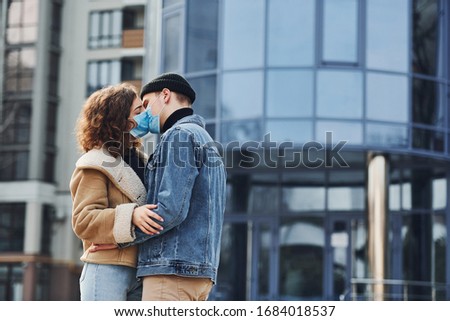 Couple in protective masks kissing each other in the city near business building at quarantine time. Conception of coronavirus.