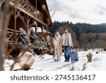 Couple pulling suitcases, walking through snow toward a wooden cabin resort for a winter vacation