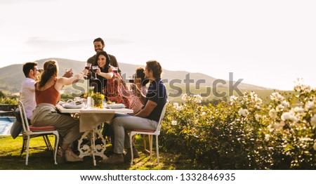 Couple raising a toast with friends sitting at table during party. Group of friends celebrating a special occasion with drinks.