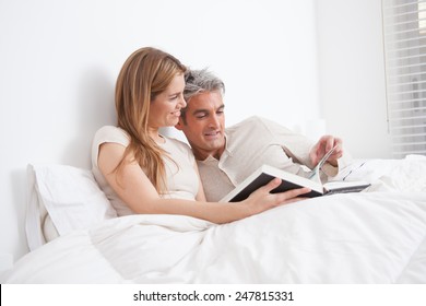 Couple Reading A Book Lying In The Bed