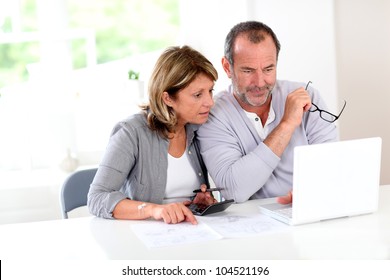 Couple reading construction plan at home with use of laptop