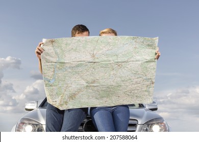 Couple Reading Map While Leaning On Car Hood During Road Trip