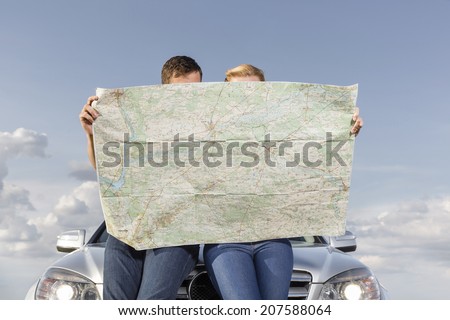 Couple reading map while leaning on car hood during road trip