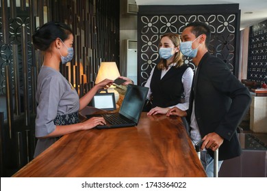 Couple and receptionist at counter in hotel wearing medical masks as precaution against virus. Young couple on a business trip doing check-in at the hotel - Shutterstock ID 1743364022