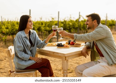 Couple relaxes at a rustic table in a sunlit vineyard, savoring wine and gourmet snacks. They share laughter and joy, surrounded by lush vines and the warmth of the evening - Powered by Shutterstock